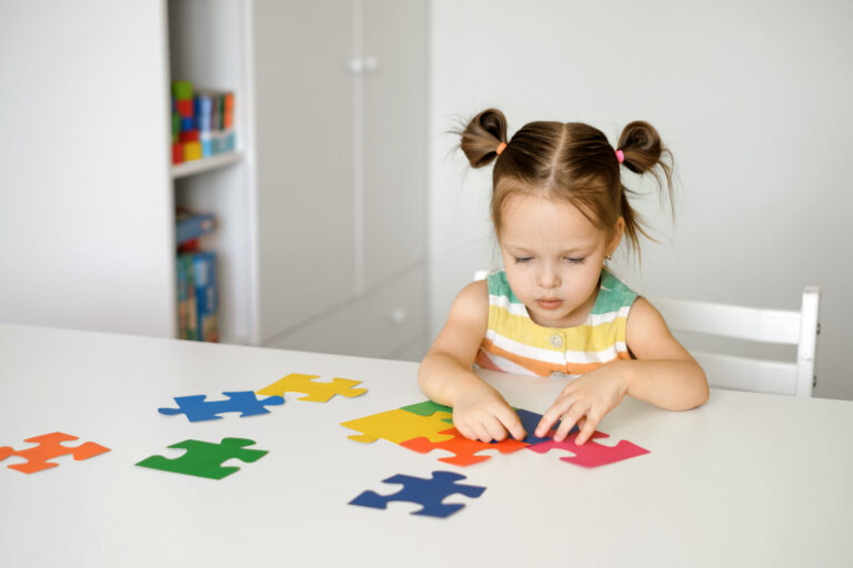 A two-year-old girl collects puzzles sitting at a table in the nursery. Puzzles are a symbol of autism. A child with mental disabilities. Preschool home development