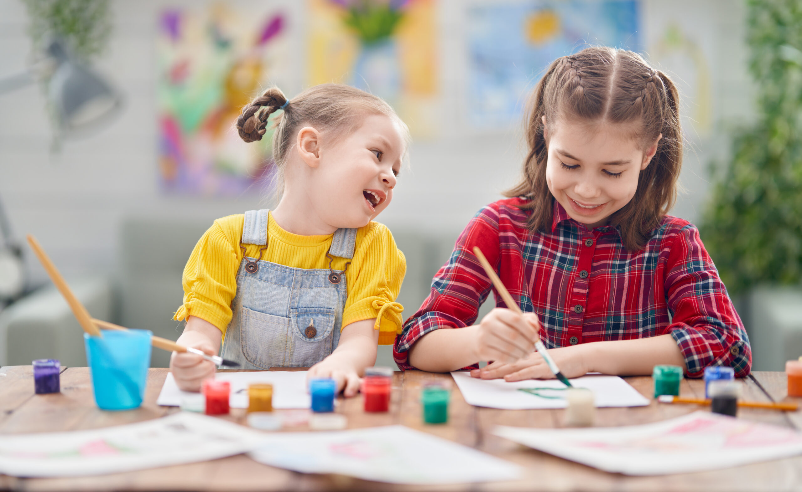 Happy kids are painting at home. The girls are being creative work sitting at the desk.